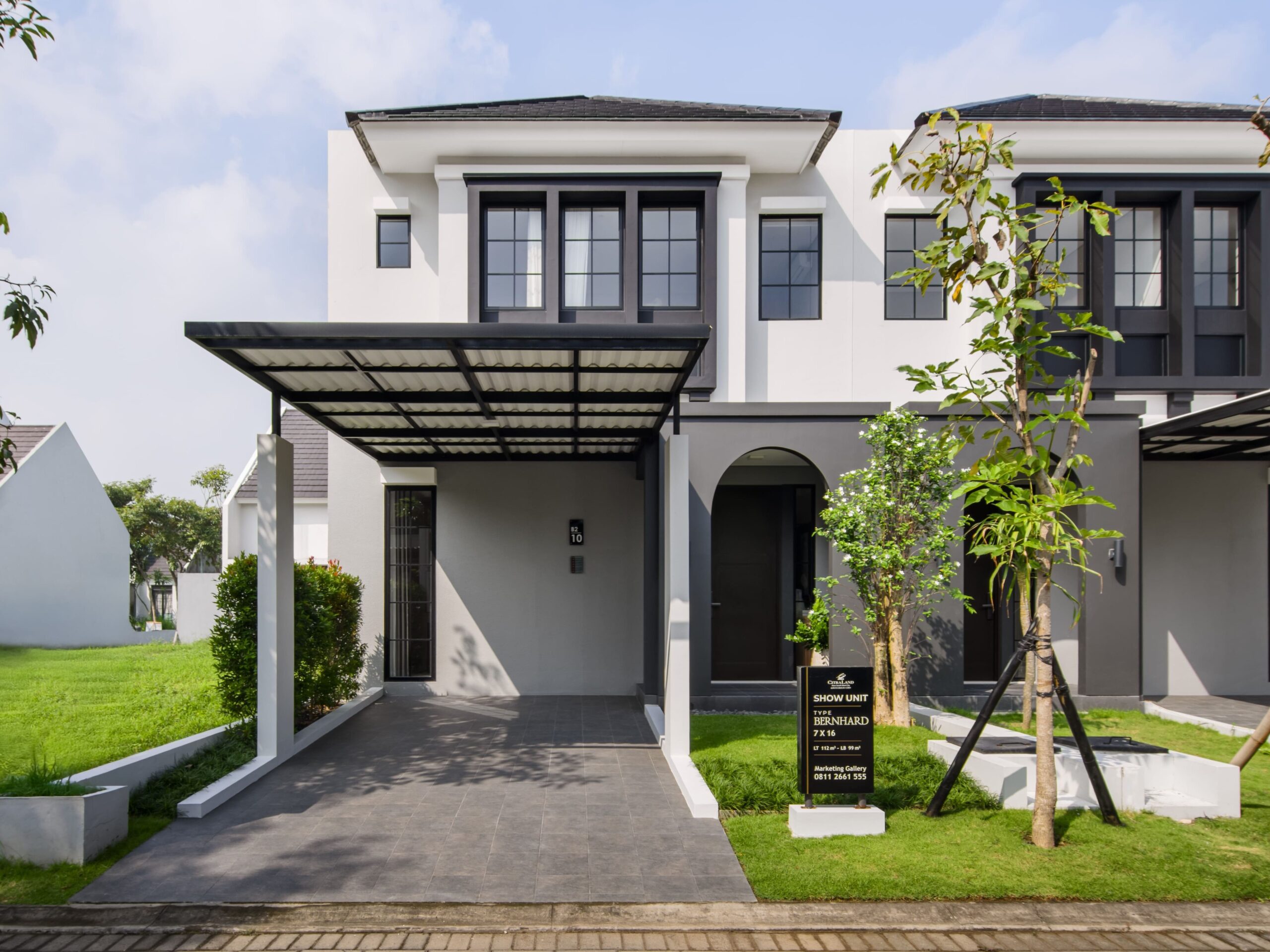 Modern townhouse row with white façades, black-framed windows, and dark canopies under a blue sky with trees in the foreground.