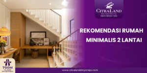 Interior of a modern minimalist two-story home with a white staircase, wooden desk, and decorative items; purple brand panel on the right reads 'REKOMENDASI RUMAH MINIMALIS 2 LANTAI' with a logo and website at the bottom.